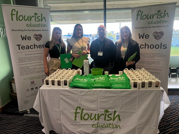 Flourish Education Recruitment Consultants standing behind their stand at the Birmingham Association of School Business Management Autumn Conference. Cupcakes on the table with green Flourish Education tote bags. Banners either side of the table with We Heart Teachers and We Heart Schools